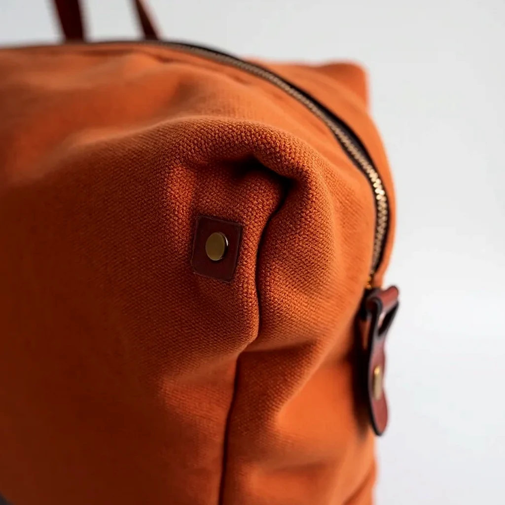 Detailed look at the waxed canvas texture in rust with a natural patina forming, a close-up of the leather trim and stitching on the messenger bag